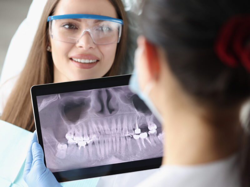 Dentist doctor examines X-ray picture on tablet screen in chair is woman patient. Dental implant installation concept